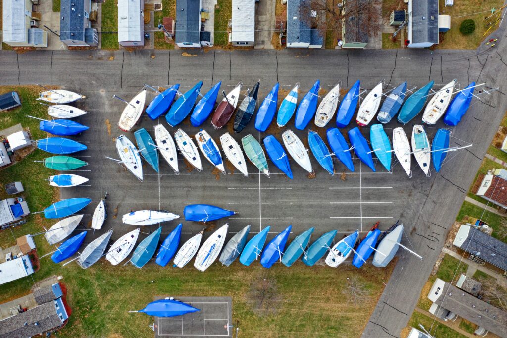 Aerial shot of numerous sailboats covered with blue tarps in an urban marina parking area.